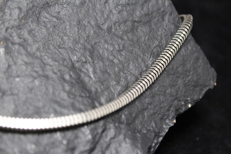 May include: A silver snake chain necklace with a smooth, shiny finish. The chain is made of small, interlocking links that create a flexible and comfortable fit.