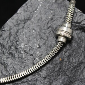May include: A silver snake chain necklace with a silver clasp. The clasp has a small diamond-like stone in the center.