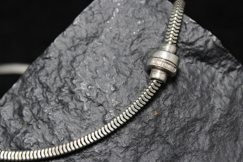 May include: A silver snake chain necklace with a silver clasp. The clasp has a small diamond-like stone in the center.