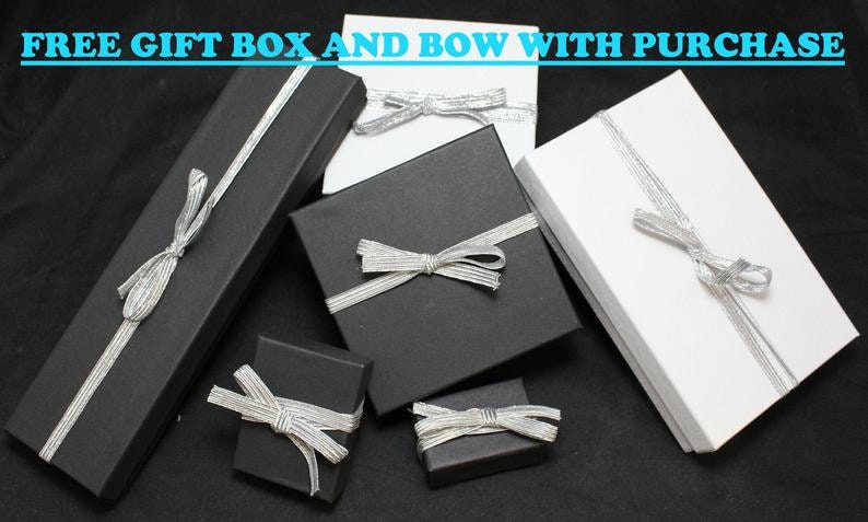 May include: Five gift boxes with silver ribbon bows. Two boxes are black and three are white. The boxes are arranged on a black surface. The text "FREE GIFT BOX AND BOW WITH PURCHASE" is at the top of the image.