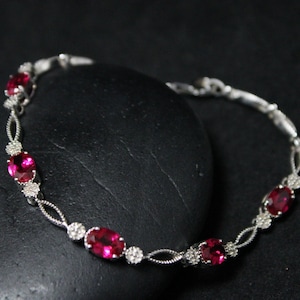 May include: A silver bracelet with a delicate chain design and five oval-shaped red gemstones.