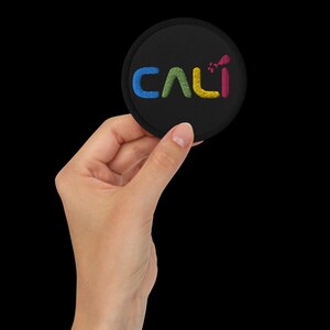 May include: A black round patch with the word "CALI" embroidered in blue, green, yellow, and red thread.