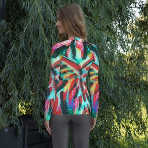 Puede incluir: Una camisa de manga larga con un estampado abstracto colorido que presenta formas geométricas y líneas atrevidas en tonos de rojo, naranja, amarillo, verde, azul y negro.