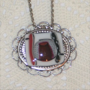 May include: A silver pendant necklace with a white and red abstract design inside a silver filigree frame.