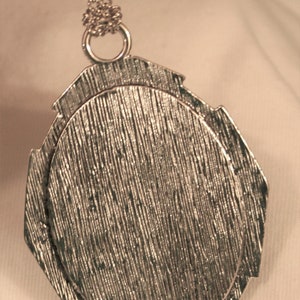 May include: Silver pendant with a textured, circular design. The pendant is attached to a silver chain.