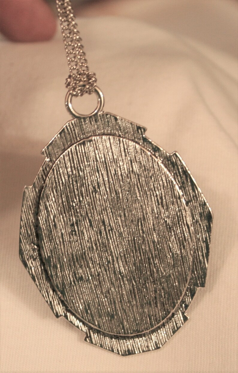 May include: Silver pendant with a textured, circular design. The pendant is attached to a silver chain.