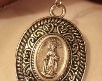 Precioso colgante con medalla devocional cristiana de Santa Dymphna en tono plateado con borde grabado en espiral.