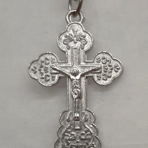 May include: A silver chain necklace with a silver cross pendant. The cross has a detailed design and a figure of Jesus Christ on it.