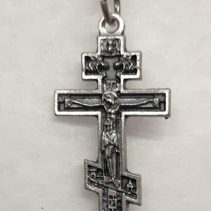 Puede incluir: Un collar de cadena de plata con un colgante de cruz de plata. La cruz está detallada con una figura de Jesucristo en la parte delantera.