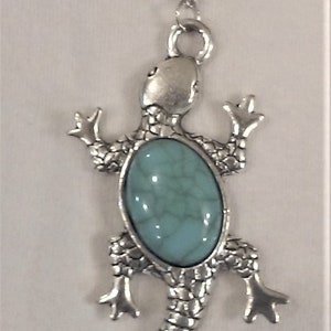 May include: A silver necklace with a turquoise and green stone lizard pendant.