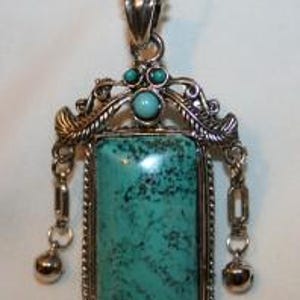 May include: A turquoise pendant necklace with a silver chain and ornate silver accents. The pendant features a rectangular turquoise stone with a silver frame and two dangling silver bells.
