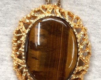 May include: A gold chain necklace with a large oval pendant featuring a brown tiger's eye stone set in a gold filigree frame.