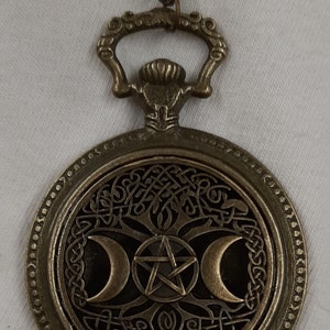 Może przedstawiać: Naszyjnik z brązu z okrągłym wisiorem przedstawiającym potrójny symbol księżyca i pentagram w węźle celtyckim. Wisiorek jest przymocowany do łańcuszka z ozdobnym oczkiem.
