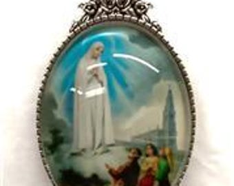 Può includere: Collana con pendente argentato con un'immagine ovale di una scena religiosa. L'immagine raffigura una donna in bianco, figure sottostanti, su uno sfondo di cielo blu e un edificio. Il pendente ha un bordo decorativo e un design a rose.