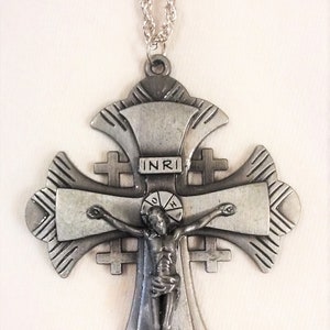 Puede incluir: Un collar con un crucifijo de metal plateado con un diseño detallado. El crucifijo presenta una figura de Jesucristo en la cruz, con la inscripción "INRI" arriba.