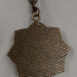 Peut inclure: Un collier avec un pendentif en bronze en forme d'&eacute;toile. Le pendentif a une surface textur&eacute;e et est attach&eacute; &agrave; une cha&icirc;ne assortie. Le collier est pr&eacute;sent&eacute; sur un fond blanc.