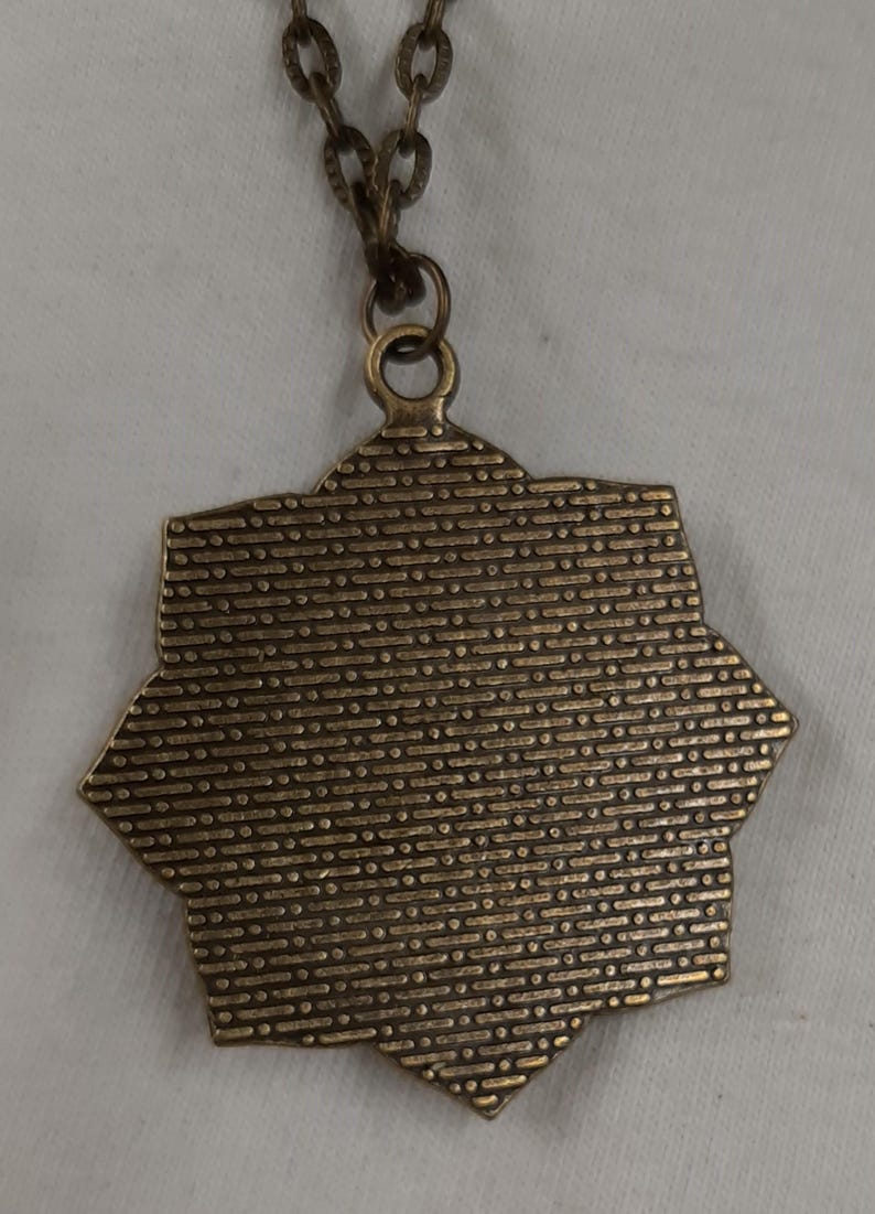 Peut inclure: Un collier avec un pendentif en bronze en forme d'&eacute;toile. Le pendentif a une surface textur&eacute;e et est attach&eacute; &agrave; une cha&icirc;ne assortie. Le collier est pr&eacute;sent&eacute; sur un fond blanc.