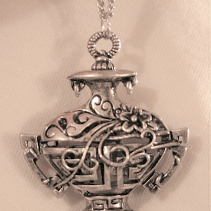 May include: A silver necklace with a detailed ornate pendant shaped like a vase with a floral design.