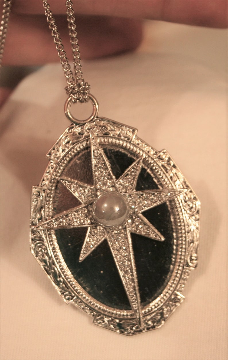 May include: A silver pendant necklace with a star-shaped design and a pearl in the center. The star is surrounded by a decorative oval frame.