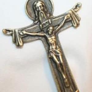 Könnte beinhalten: Ein detaillierter metallischer Kreuzanhänger mit einer goldfarbenen Kette. Das Kreuz zeigt eine Darstellung von Jesus Christus am Kreuz, mit einer von einem Heiligenschein umgebenen Figur darüber. Der Anhänger ist wahrscheinlich aus einer Metalllegierung gefertigt und für religiösen Gebrauch bestimmt.