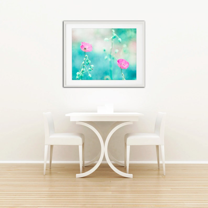 May include: A white table with two white chairs in front of a framed print of two pink flowers on a blue background.