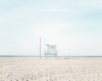 May include: A white lifeguard stand with the number 14 on the side, on a sandy beach with a blue ocean in the background.