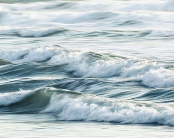 May include: A close-up of ocean waves crashing and breaking, creating a white foamy texture against the blue water.
