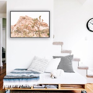 May include: A framed photograph of a desert landscape with a rocky mountain and Joshua trees. The photo is hanging on a white wall above a wooden pallet bed with white bedding and a blue and white blanket.