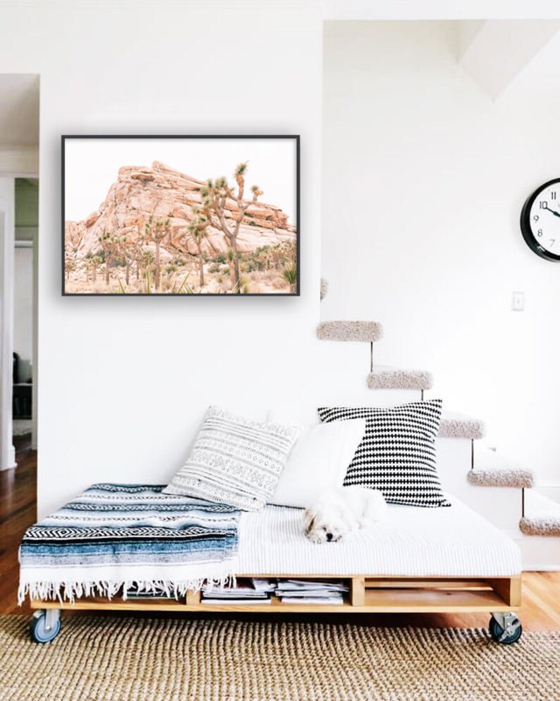 May include: A framed photograph of a desert landscape with a rocky mountain and Joshua trees. The photo is hanging on a white wall above a wooden pallet bed with white bedding and a blue and white blanket.