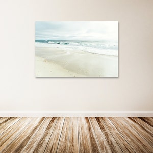 May include: A photograph of a beach scene with white sand and blue waves crashing on the shore. The sky is a light blue with some clouds.