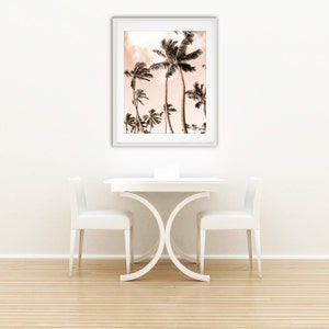 May include: A white dining table with two white chairs and a framed print of palm trees against a pink sky. The table has a unique X-shaped base.