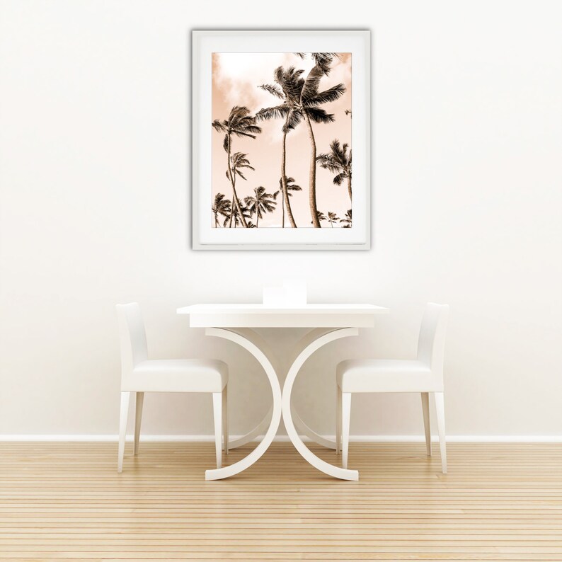 May include: A white dining table with two white chairs and a framed print of palm trees against a pink sky. The table has a unique X-shaped base.