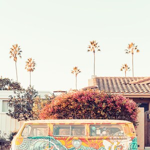 May include: A vintage yellow van with colorful psychedelic artwork featuring a peace sign, a sun, and waves. The van is parked on a street with palm trees in the background.