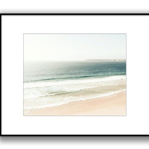 May include: A panoramic view of a sandy beach with turquoise ocean waves crashing on the shore. The horizon is a hazy white, and a distant landmass is visible in the background.