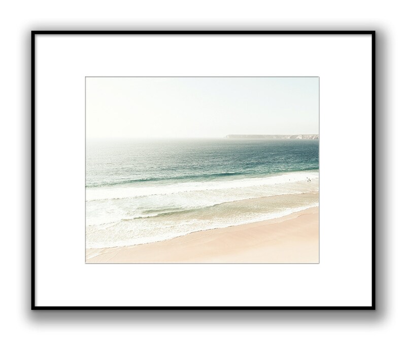 May include: A panoramic view of a sandy beach with turquoise ocean waves crashing on the shore. The horizon is a hazy white, and a distant landmass is visible in the background.