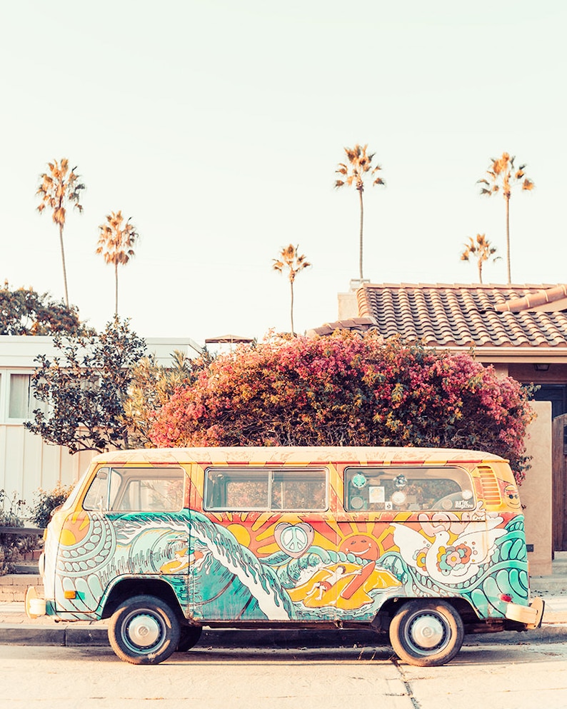 May include: A brightly colored, vintage Volkswagen van with a psychedelic paint job featuring waves, suns, and peace signs. The van is parked on a street with palm trees in the background.