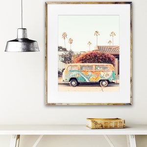 May include: A vintage yellow Volkswagen bus with colorful psychedelic paint, parked on a street with palm trees in the background. The bus has a peace sign painted on the side.