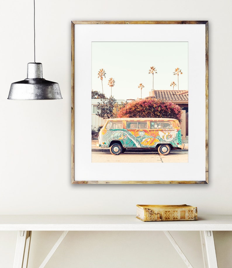 May include: A vintage yellow Volkswagen bus with colorful psychedelic paint, parked on a street with palm trees in the background. The bus has a peace sign painted on the side.