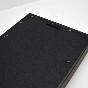 May include: The back of a black canvas print with a hanging mechanism and staples holding the canvas to the frame.