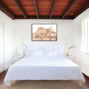 May include: A white bed with white bedding and pillows in a bedroom with a wood ceiling. A framed photograph of a desert landscape with a rocky mountain and Joshua trees hangs above the bed.
