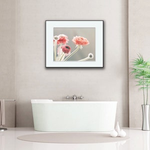 May include: A framed photograph of pink flowers in a white frame against a white wall. The photo is hanging above a white bathtub in a bathroom.