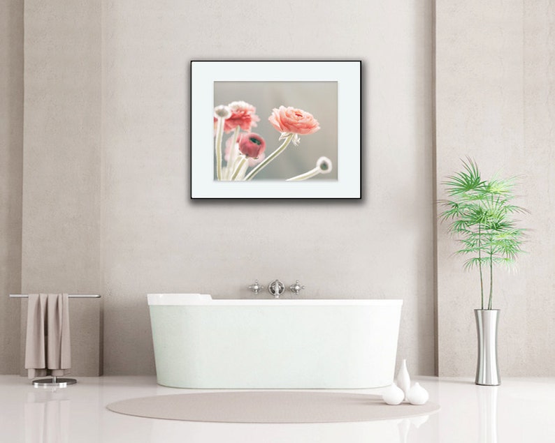 May include: A framed photograph of pink flowers in a white frame against a white wall. The photo is hanging above a white bathtub in a bathroom.