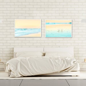 May include: Two framed beach scene prints with a white background and a white bed in the foreground.