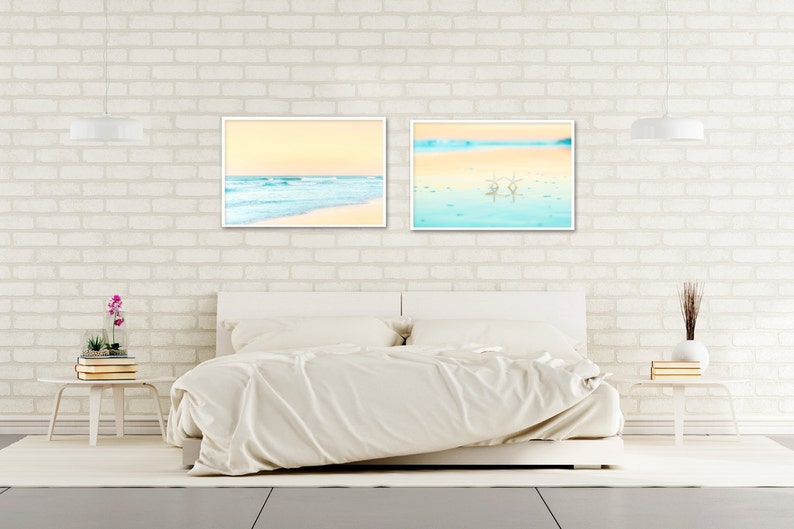 May include: Two framed beach scene prints with a white background and a white bed in the foreground.