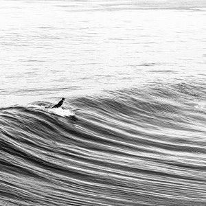 May include: A surfer rides a wave in the ocean. The surfer is wearing a wetsuit and is paddling with their arms. The wave is breaking and the water is white and foamy.