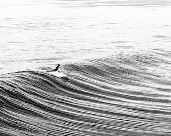 May include: A surfer rides a wave in the ocean. The surfer is wearing a wetsuit and is paddling with their arms. The wave is breaking and the water is white and foamy.