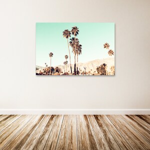 May include: A photograph of a row of palm trees against a light blue sky and a mountain range in the background. The palm trees are silhouetted against the sky and the mountains.