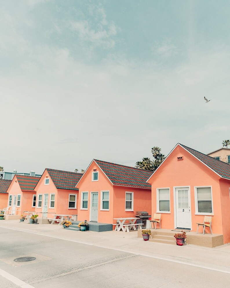 May include: A row of five pastel pink beach houses with white trim and red tile roofs. The houses have white doors and windows. There are potted plants and outdoor furniture in front of the houses.