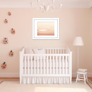 May include: A white crib with a white ruffle skirt and a white blanket. The crib is in a nursery with a white lamp and a framed print of a seashell on the wall. There are several ladybug decorations on the wall.