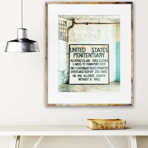 May include: A black and white photograph of a sign that reads "United States Penitentiary" with the text "Alcatraz Island Area 12 Acres 1 1/2 Miles to Transport Dock Only Government Boats Permitted Others Must Keep Off 200 Yards No One Allowed Ashore Without A Pass".
